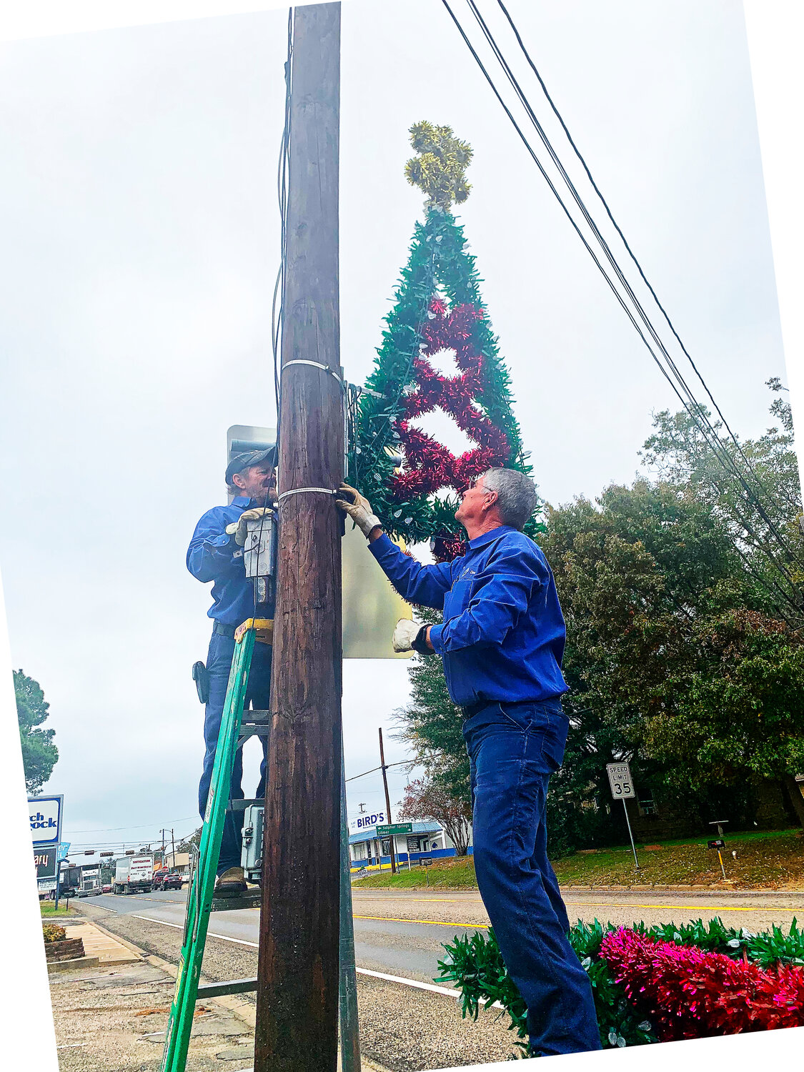 Dee Gilbreath and Mitch Walls place holiday decorations along Main St. in Quitman last week. (Monitor photo by Lesa Major)